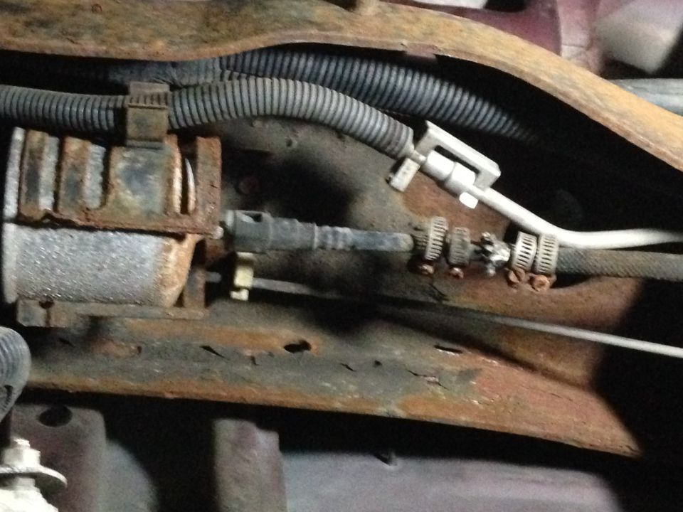Undercarriage of a vehicle showing rusty frame, fuel lines, and hoses