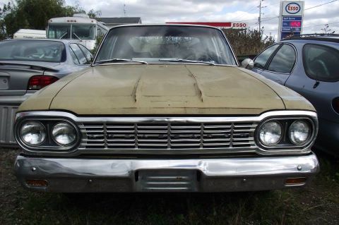 1964 AMC Javelin - This sedan features a prominent chrome grille and dual headlights, with other vehicles and a bus in the background.
