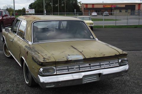 1964 AMC Javelin - A weathered sedan sits in a lot, showing its chrome grille and taillights.