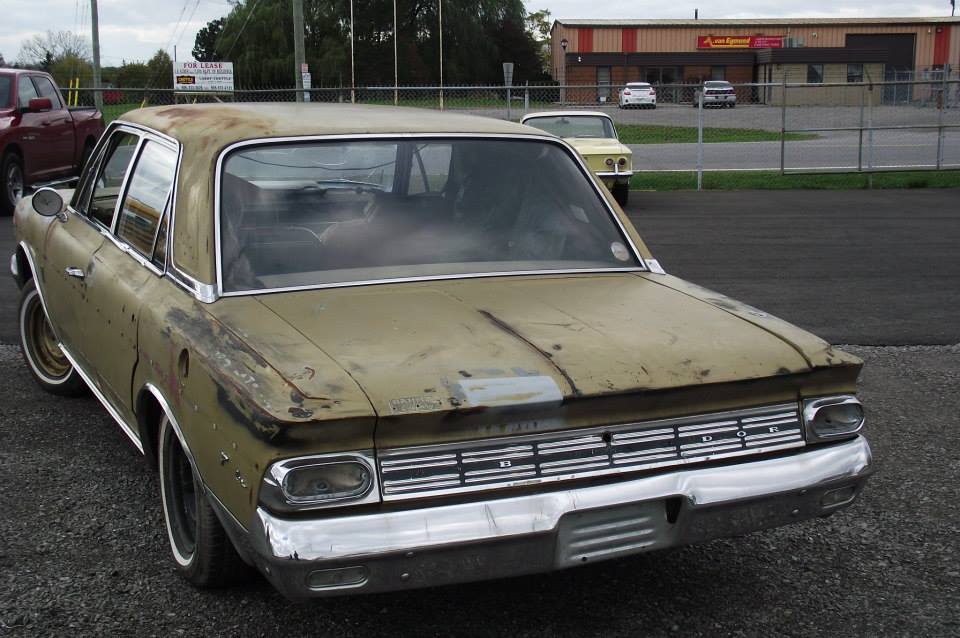 Old tan sedan, rear view. Another car is parked behind it
