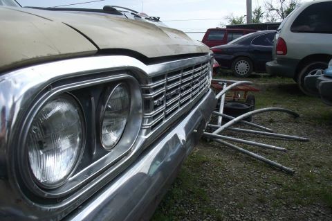 1964 AMC Javelin - A close-up of a vintage car's front end, showing its grille and headlights, with other vehicles parked nearby.