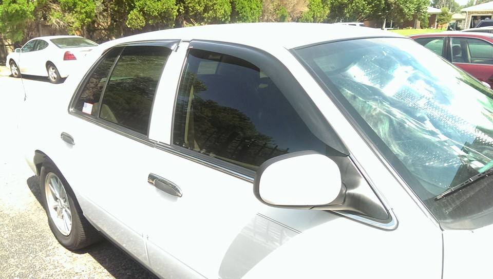 White sedan parked outside, side view. Another white car is in the background