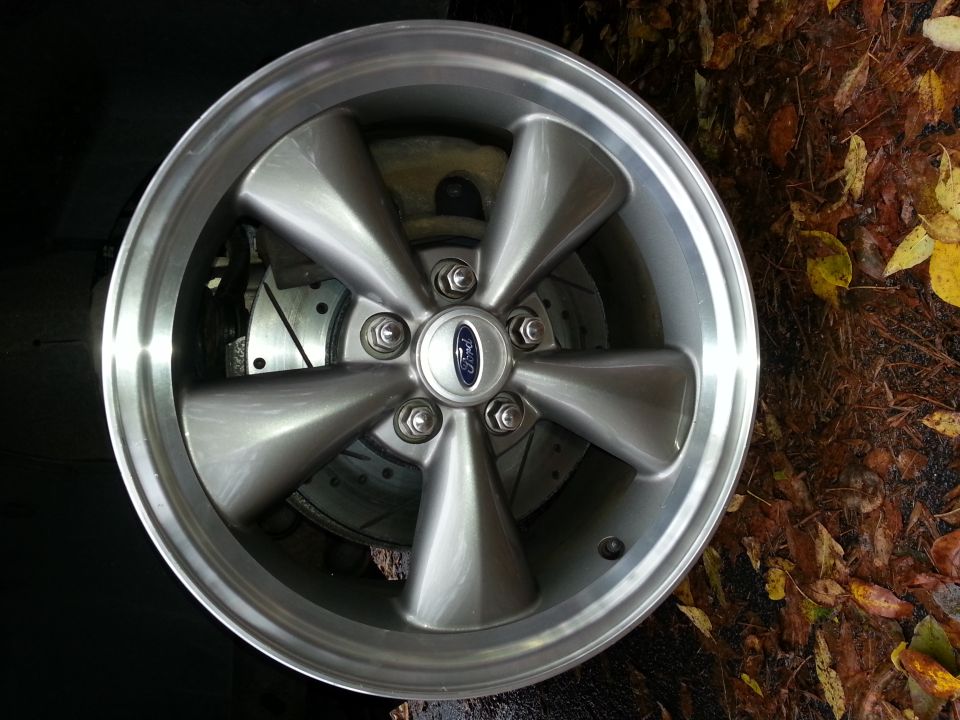 Close-up of a silver five-spoke wheel with a Ford logo center cap and a slotted brake rotor visible behind it