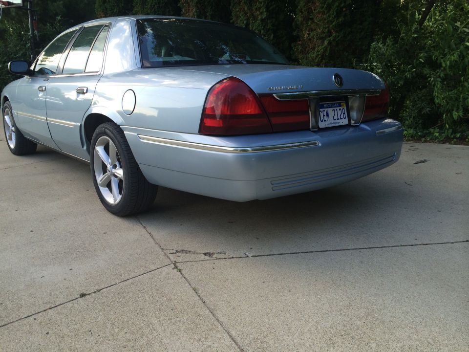 Light blue 2003 Mercury Grand Marquis sedan, rear 3/4 view, parked on concrete driveway