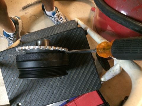 1996 Ford Bronco - A person is using a screwdriver on a crankshaft pulley with a gear attached.