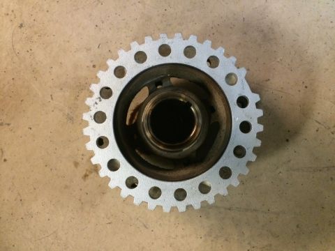 1996 Ford Bronco - A metal crankshaft pulley with a toothed outer edge and circular holes is shown against a textured surface.