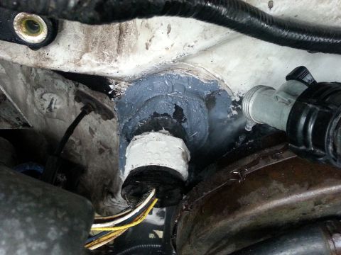 1992 Ford Bronco - Close-up of a firewall grommet, sealed with sealant, with visible wiring and a hose.
