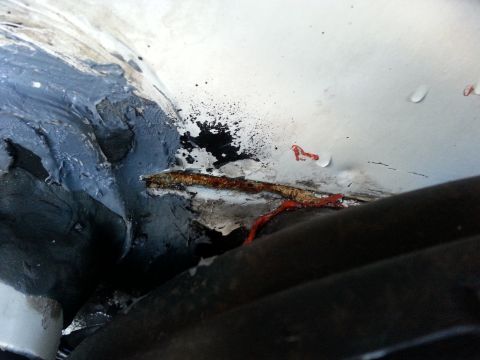 1992 Ford Bronco - Close-up of a rusted metal seam with sealant and red fluid, possibly indicating a leak.