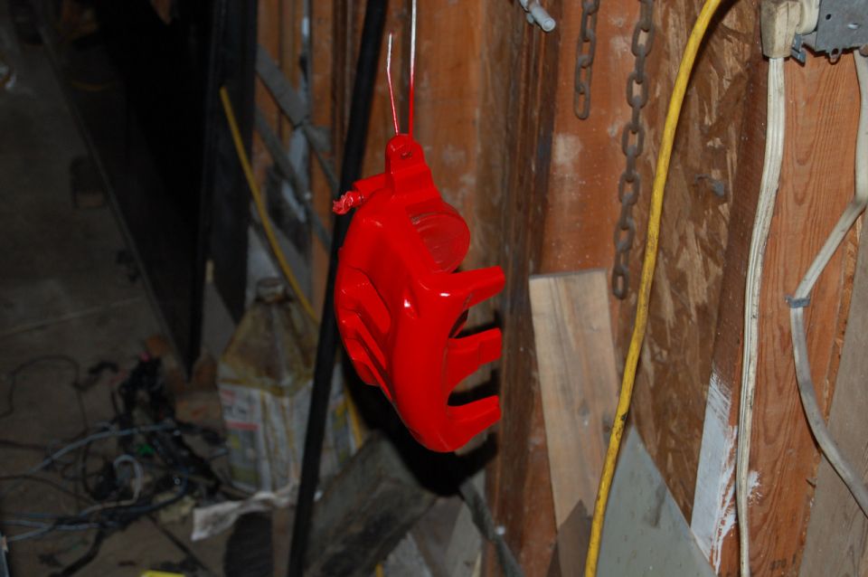 Red painted car part hanging from wire, with Supermotors logo at bottom right