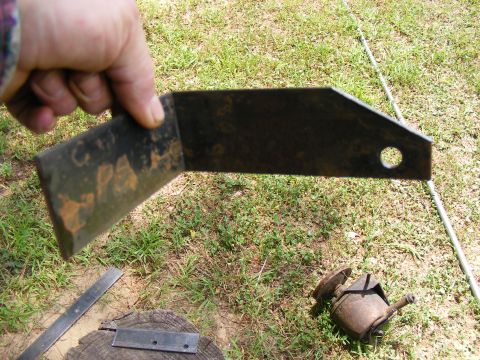 Rusty metal bracket with a hole, held by a hand over grass