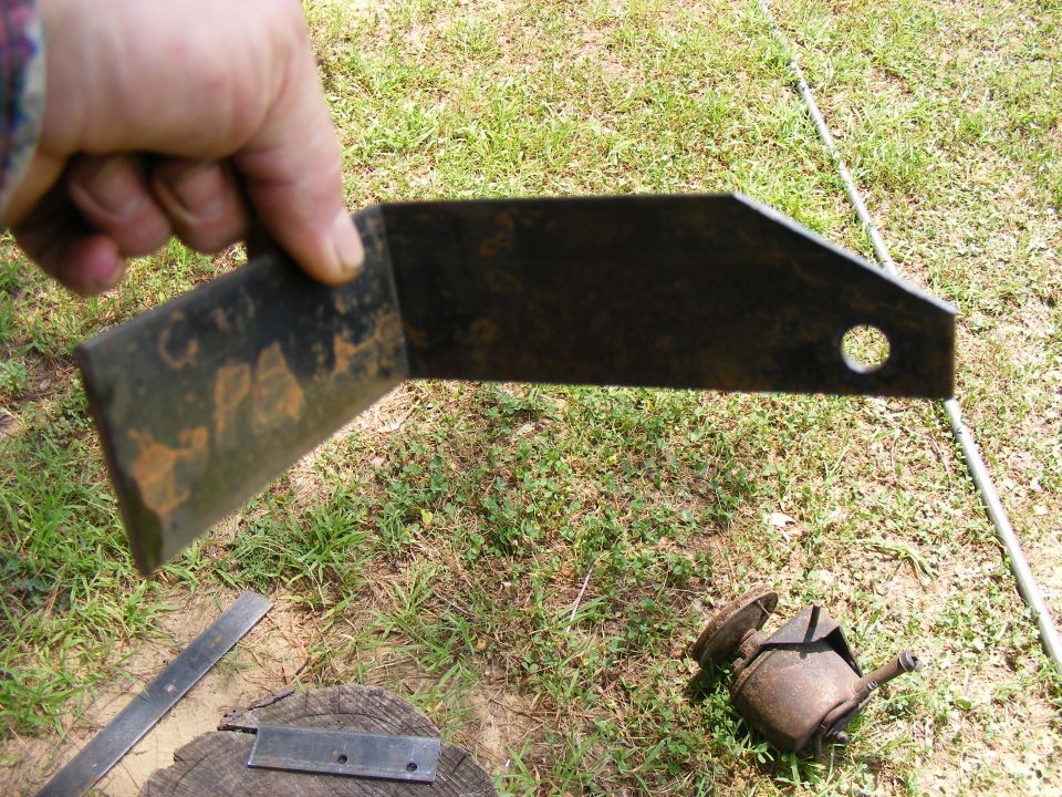 Rusty metal bracket with a hole, held by a hand over grass