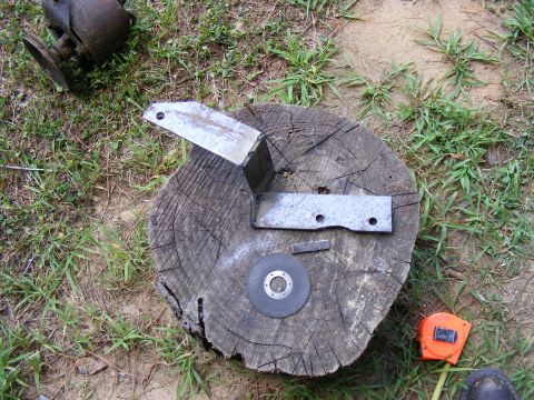 Metal bracket pieces and a cutting disc on a log. Tape measure nearby