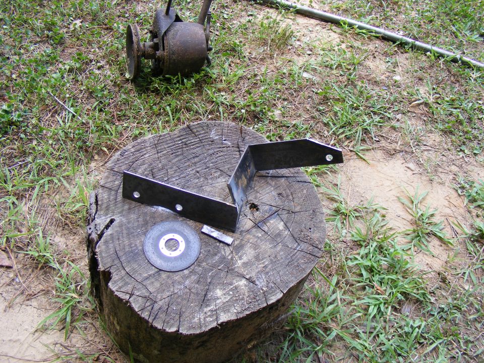 Metal bracket and cutting wheel on a tree stump. Old rusty engine part in background