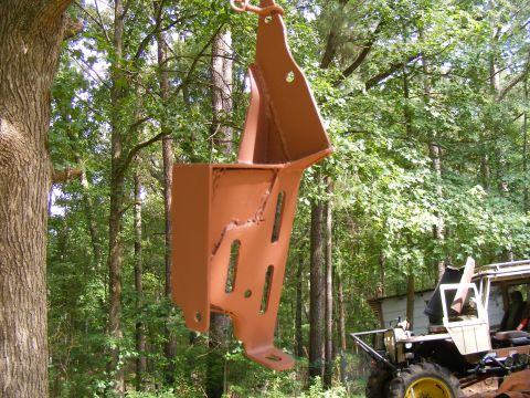 Rusted metal bracket hanging from a chain, with trees and a building in the background