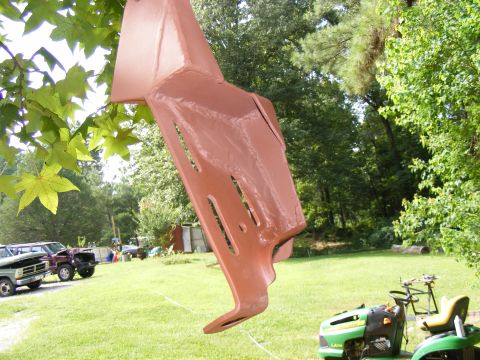 Painted metal part hanging from a tree branch. In the background, a few trucks and a riding mower are parked o