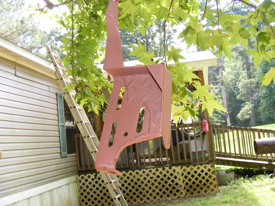 Painted metal bracket hanging from tree branch, with ladder and house in background