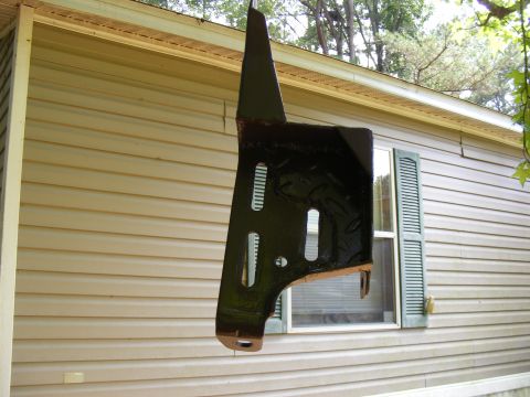 Black metal part hanging in front of a house with a "SUPERMOTORS.NET" watermark