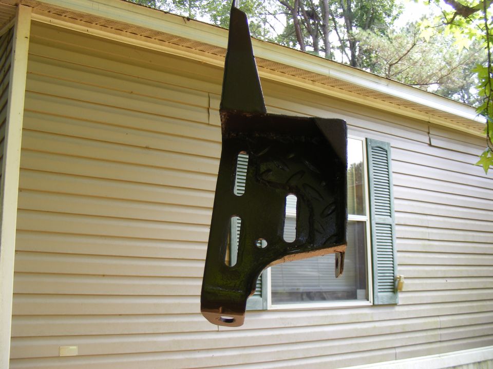 Black metal part hanging in front of a house with a "SUPERMOTORS.NET" watermark