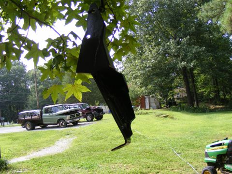 Two trucks parked in a yard, one is a flatbed and the other is a darker pickup. A lawnmower is in the foregrou