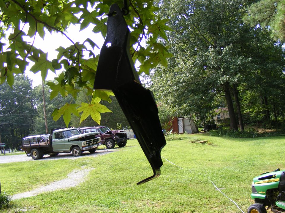 Two trucks parked in a yard, one is a flatbed and the other is a darker pickup. A lawnmower is in the foreground