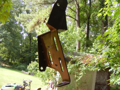 Metal bracket hanging outdoors, showing rust and mounting holes