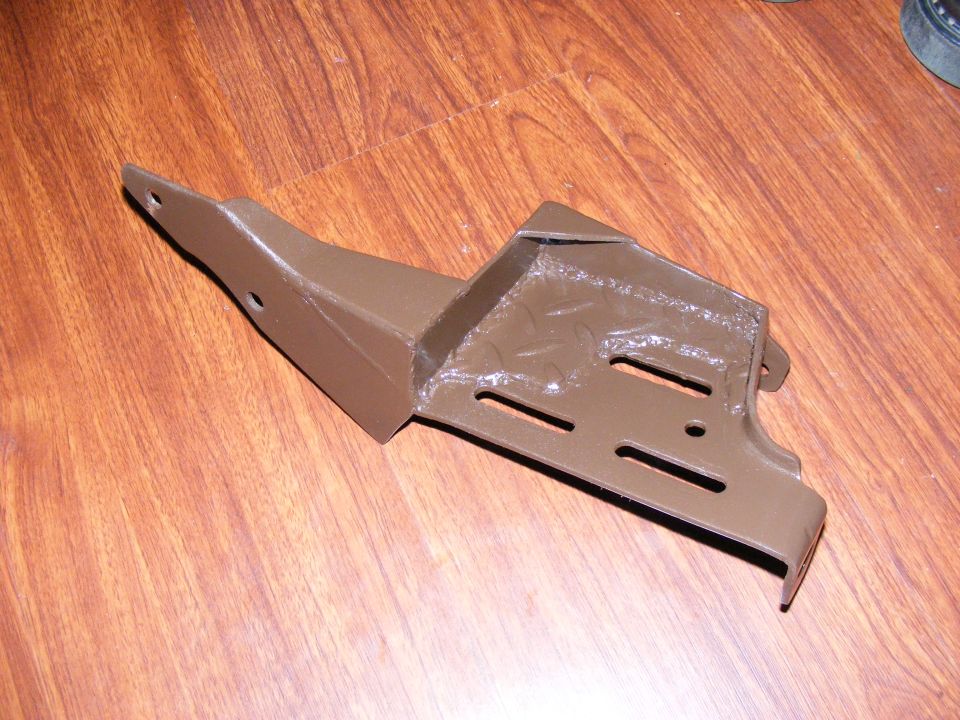 Brown metal bracket with multiple slots and holes, on a wooden floor