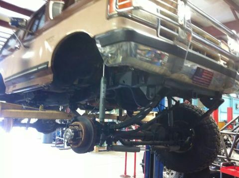 1988 Ford Bronco - Underside view of a lifted brown Ford Bronco undergoing maintenance.