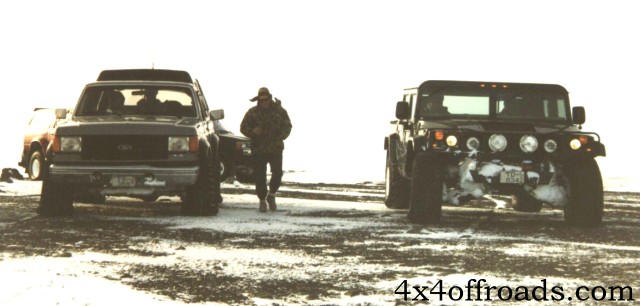 Gray Ford pickup and black Hummer parked on snowy ground with a person walking between them