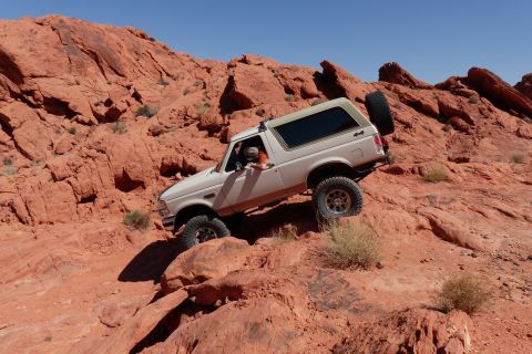 1995 Ford Bronco - A white Ford Bronco navigates a steep, red rock trail under a clear blue sky.