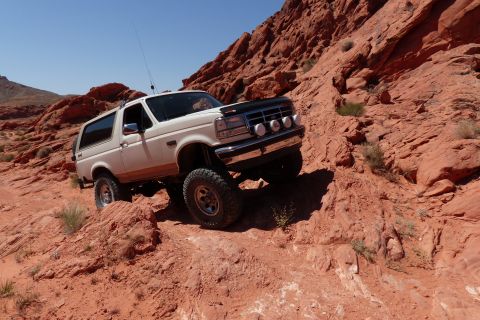 1995 Ford Bronco - A white 1995 Ford Bronco navigates a challenging off-road trail through a desert landscape.