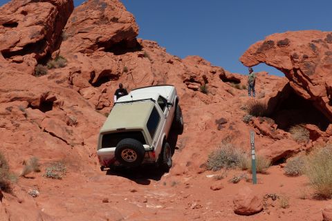 1995 Ford Bronco - An SUV navigates a challenging off-road path through a red rock landscape under a clear blue sky.