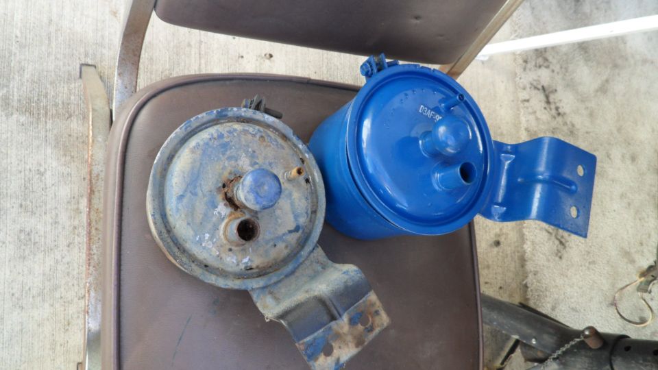 Two fuel filters, one rusty and blue, the other freshly painted bright blue, rest on a brown seat