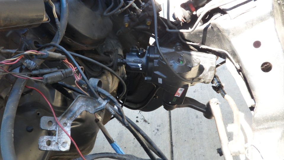 Close-up of a vehicle's steering gear box and linkage, with wiring harness visible