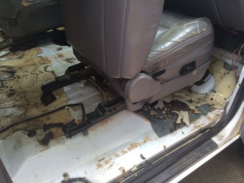 1994 Ford Bronco - The interior of a vehicle shows significant wear and tear, with a damaged seat and corroded floor.