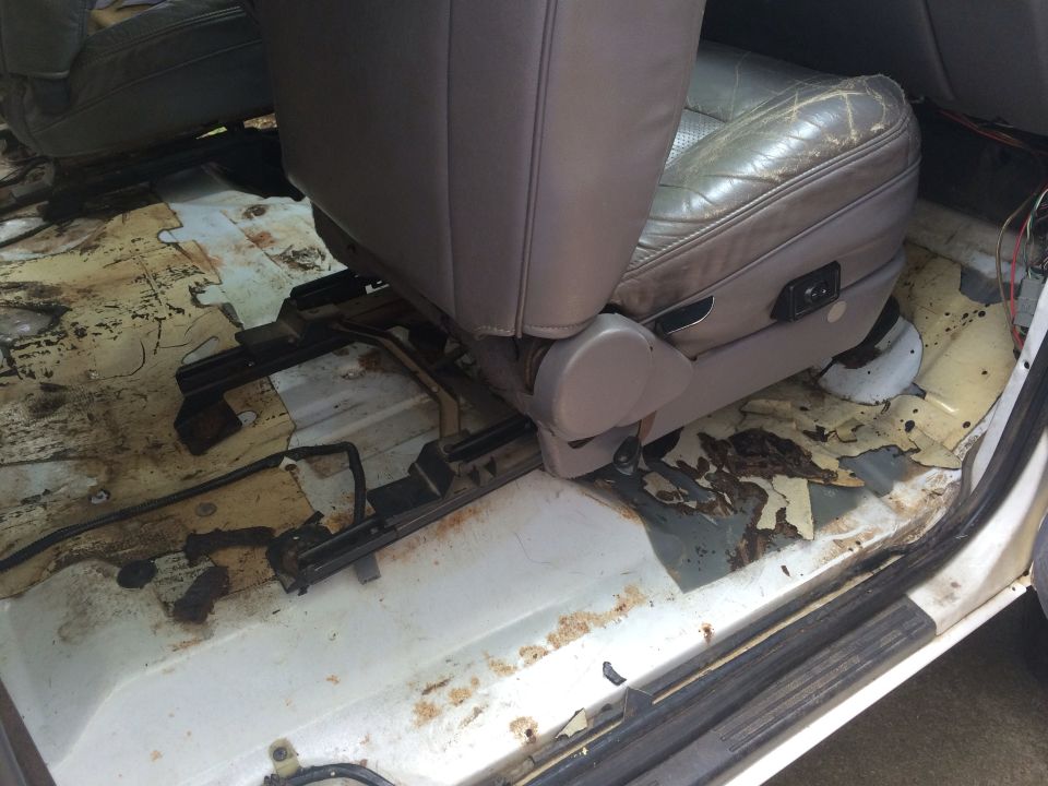 Car interior with torn leather seat and rusted floor panels