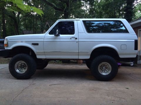 1994 Ford Bronco - Side view of a lifted white Ford Bronco with tinted windows and aftermarket wheels.