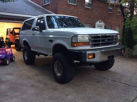 1994 Ford Bronco - White 1994 Ford Bronco with aftermarket wheels and tires parked outside a brick house.