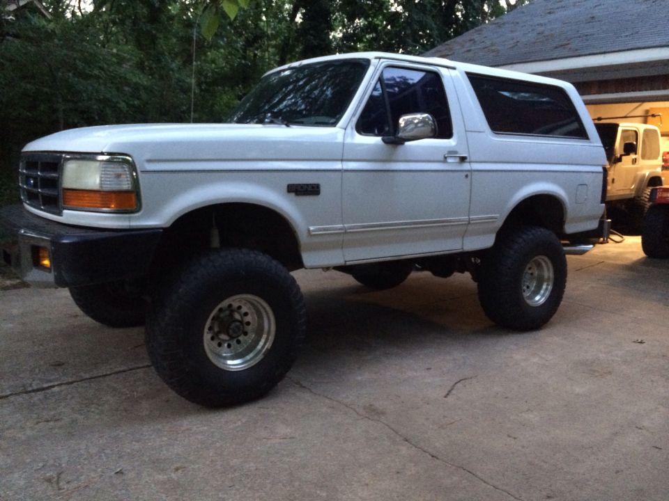 White lifted Ford Bronco parked outside a garage, another vehicle visible behind it