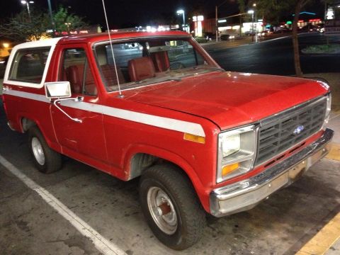 1982 Ford Bronco - This red and white Ford Bronco features a prominent chrome grille and a distinctive white stripe along its side.