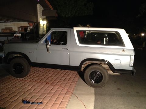 1982 Ford Bronco - This gray Ford Bronco with a white top is seen from the side, parked on a brick surface at night.