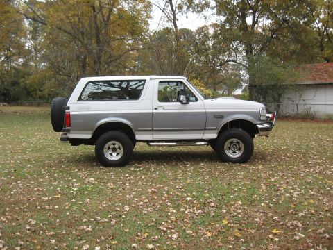 1994 Ford Bronco - This Ford Bronco is parked outside on a fall day, with trees and a building in the background.