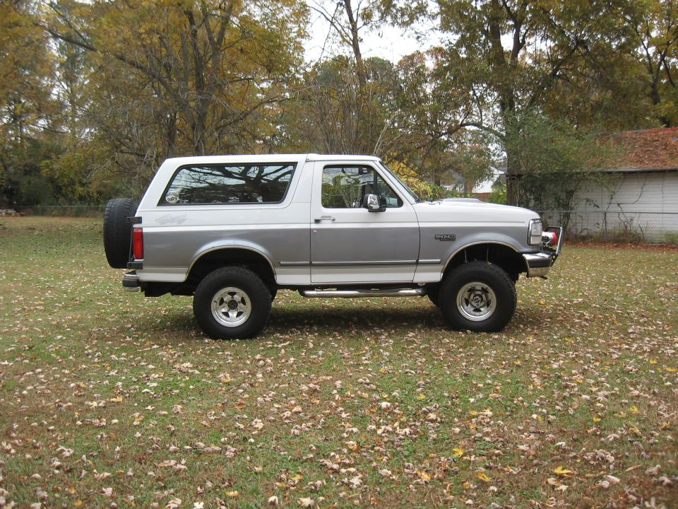 Side view of a two-tone silver and white Ford Bronco parked on a grassy lawn with fallen leaves