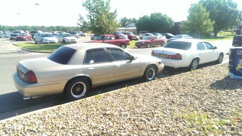 2000 Mercury Grand Marquis - Two sedans, one gold and one white, are parked side-by-side on a street.