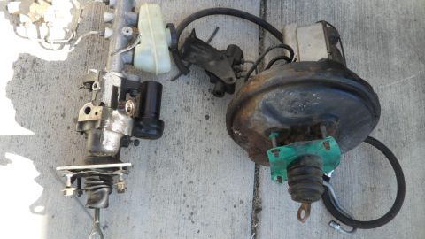 1972 Ford Ranchero - Two automotive brake system components, a master cylinder and a brake booster, are laid out on a concrete surface.