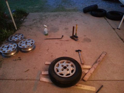 1991 Ford Festiva - Tools and spare wheels are gathered on the ground, possibly for a tire change or repair.