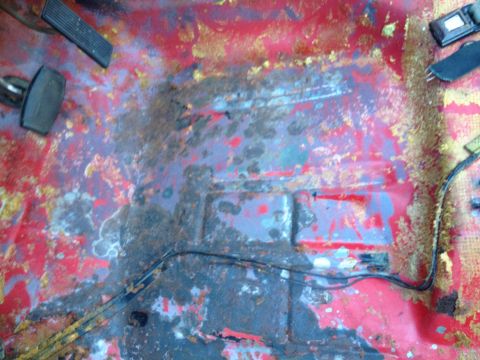1978 Ford Bronco - The floor of a vehicle shows significant rust and discoloration, with pedals visible.