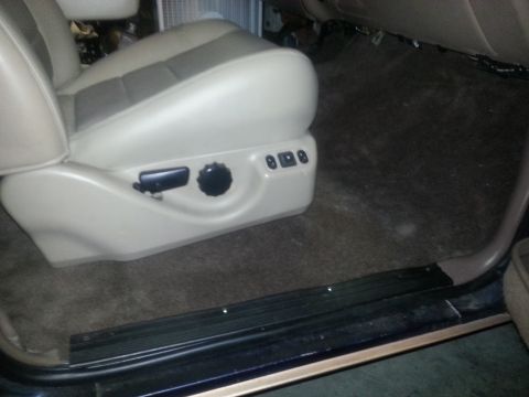1994 Ford Bronco - Close-up of a vehicle's power seat base and surrounding carpet, with adjustment knobs and buttons visible.