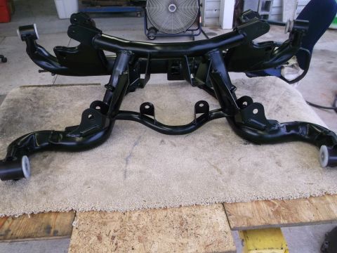 1967 Ford Mustang - A black metal suspension subframe, likely for a classic car, is displayed on a rug.
