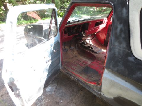 1978 Ford Bronco - The interior of a vehicle is visible with the driver's side door ajar, revealing the red dashboard and floor.