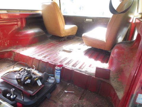 1978 Ford Bronco - The interior of a red vehicle shows tan seats and a cargo area with tools and a spray can.
